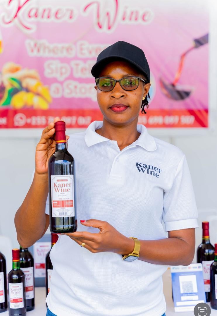A person in a Kaner Wine shirt holding a wine bottle